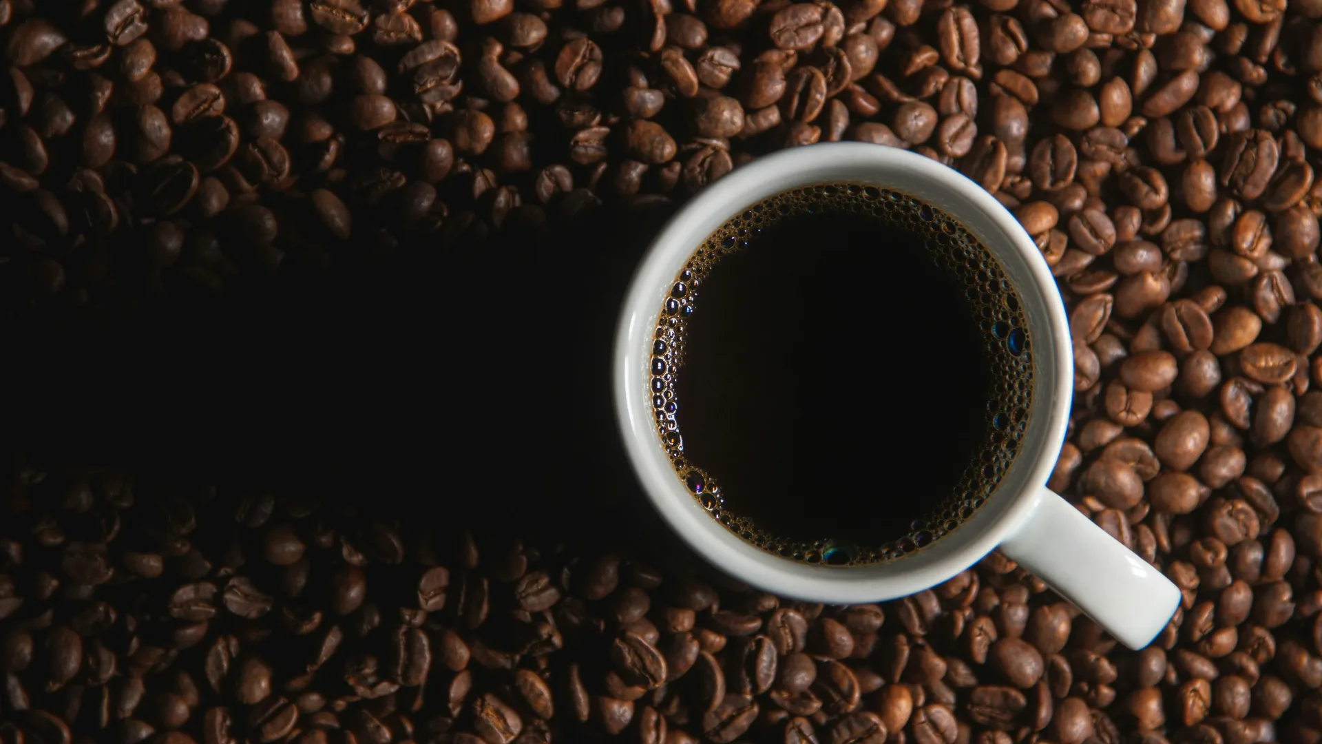 Fresh coffee beans beside a cup and pastry on a cafe table