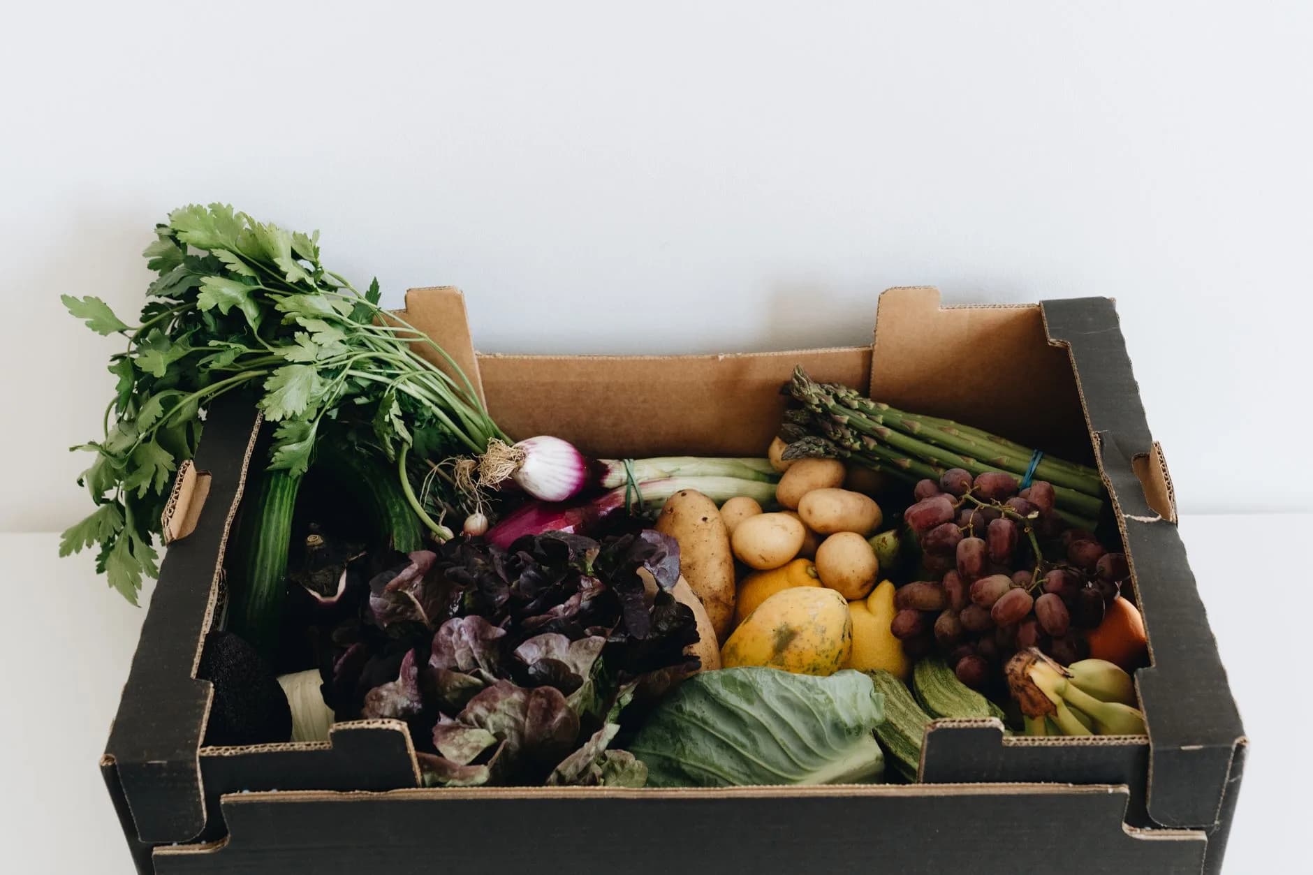 A delivered vegetable box with fresh produce arranged for unpacking at home.